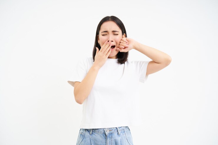 無料Photo 疲れ果てた女子学生の女の子があくびをし、疲れて立っている白いスタジオの背景に眠そうに見える