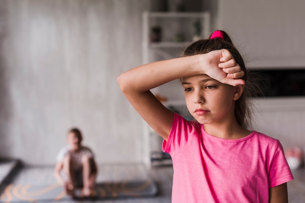 Free photo exhausted girl with her hand on forehead standing in front of blurred boy at background