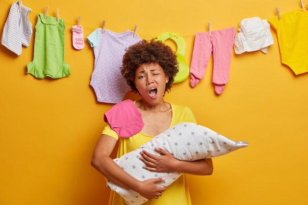 Free photo exhausted mother yawns and wants to sleep, poses with newborn baby wrapped in blanket, tired of doing domestic chores, has much work as cares about infant. parenthood, tiredness and moterhood