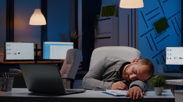 スタートアップビジネスオフィスの机のテーブルで寝ている疲れ果てた過労ビジネスマン