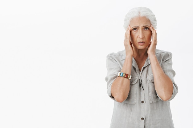 Exhausted sad grandmother touching head, complaining headache, have migraine