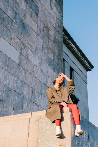 Free photo exhausted stylish young woman sitting on wall