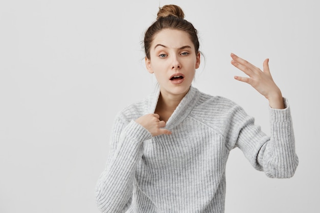 Exhausted woman gesturing with hand being warm pulling off her sweater. Female shopper feeling heat standing in queue while making purchases at trade mall. Body language