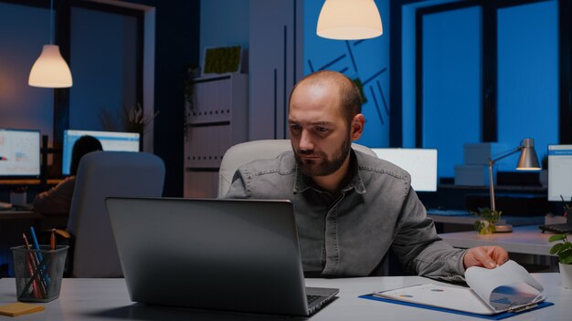 Exhausted workaholic businessman analysing marketing statistics sitting at desk table