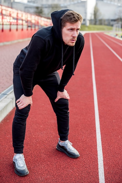 Exhausted young male athlete standing on race track