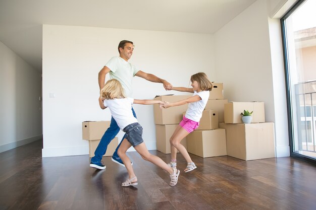 Exited father round dancing with two girls among unpacked boxes