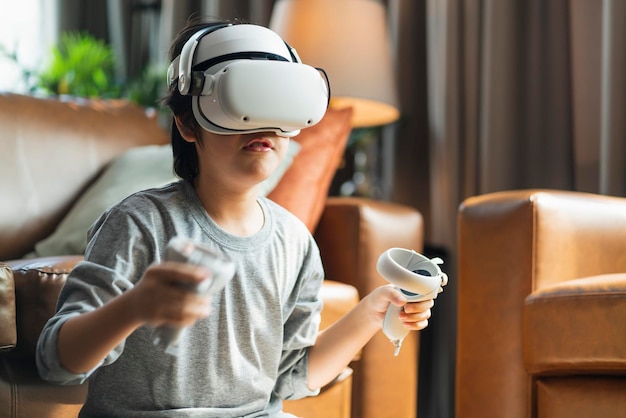 終了するアジアの子供男性の男の子は、VRテクノロジーを使用してホームホームテクノロジーの若いティーンのリビングルームでオンラインでスポーツゲームをプレイするコントロールハンドル付きのウェアラブルVRヘッドセットでメタバースゲームを楽しんでいます