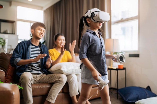 Exiting daugther wear vr headset playing virtual gaming sport innovation while her parent sit and cheering together on sofa counh living room at homeasian family spending fun moment weekend activity