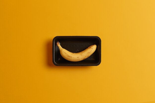 Exotic ripe banana fruit packed on tray for sale in supermarket, isolated over yellow background. Tasty yummy healthy snack. Dieting organic food concept. Summer vitamin diet. Horizontal shot