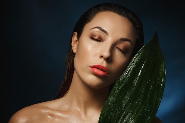 Exotic style. Fashion photography. Naked woman leaning to green plant.