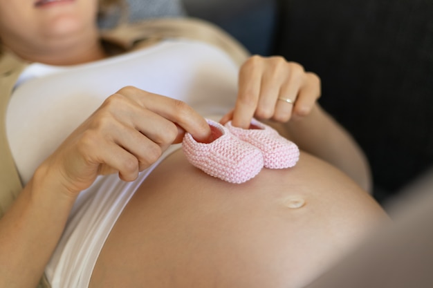 Expectant mother applying pink baby shoes to big naked belly