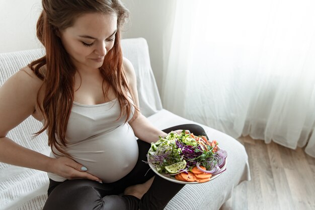 The expectant mother in the last months of pregnancy is holding a plate of vegetable salad.