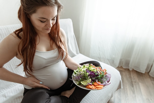 妊娠の最後の数ヶ月の妊婦は、野菜サラダのプレートを持っています。