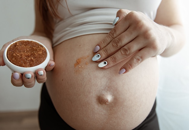 Free photo the expectant mother rubs a natural scrub into the skin of her abdomen for skin care and stretch marks.