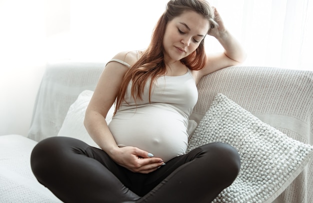 大きなお腹を抱えた妊婦が自宅のソファに座っている。