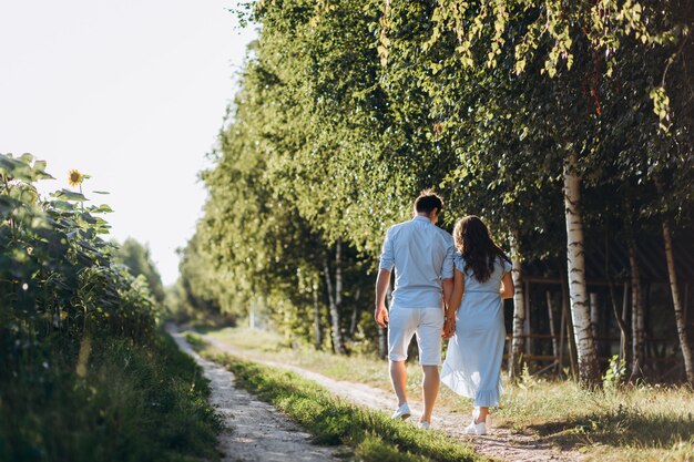 Expecting man and woman walk along the path across the field with sunflowers