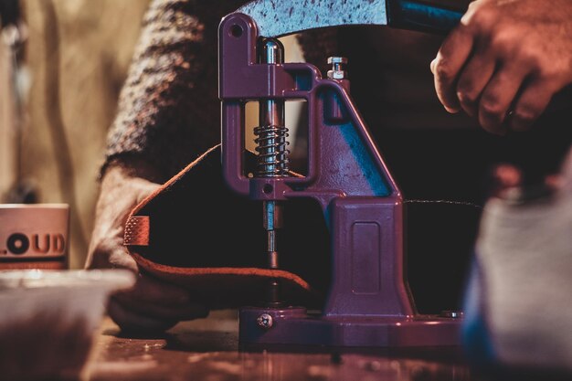 Experienced shoes master is making holes for laces in shoes using special tool.