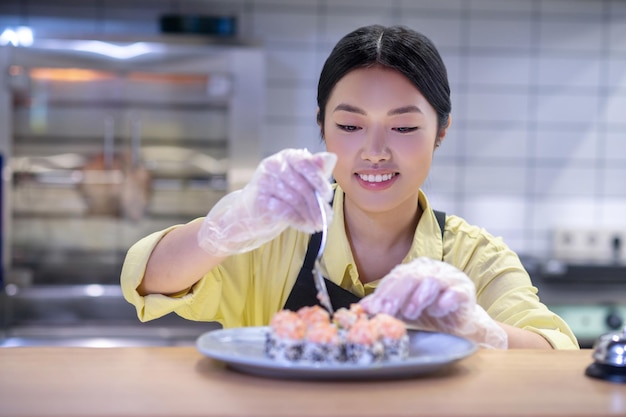 Опытный суши-повар. Азиатка кладет суши на тарелку и выглядит вдохновленной