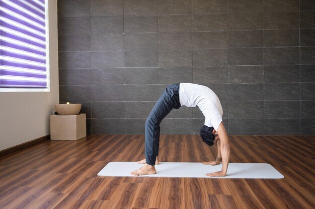 Experienced yogi doing wheel yoga pose in gym