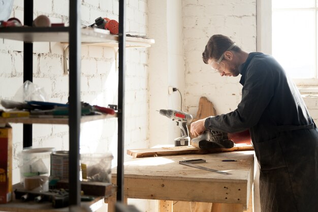 Experienced young carpenter working with wood at joinery workshop indoors