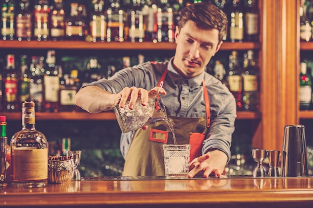 Expert barman is making cocktail at night club.