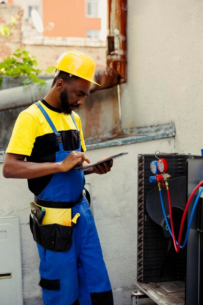 Expert repairman doing condenser investigations, filter replacements and necessary fixes to prevent major breakdowns. Proficient worker checking up hvac system, writing findings on clipboard