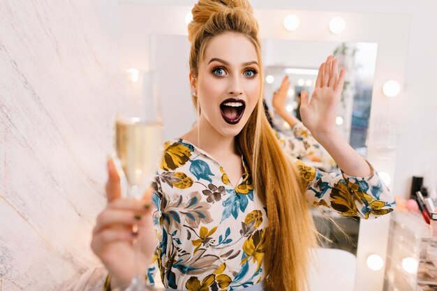 Expressing brightful emotions of stylish pretty model with luxury coiffure, beautiful makeup, glass of champagne in hairdresser salon