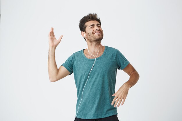 Expressive smiling handsome young spanish man in blue t-shirt, listening his favourite song with headphones and dancing happily. People and lifestyle concept