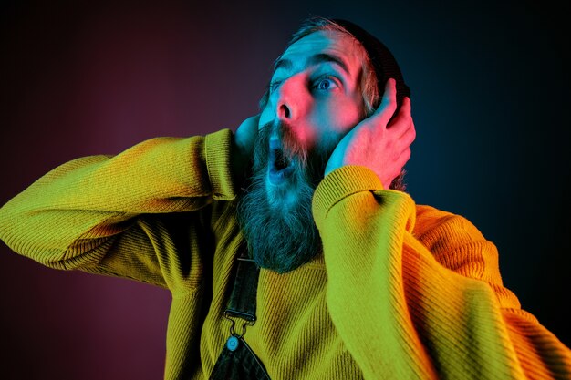 Exremely shocked, astonished. Caucasian man's portrait on gradient studio background in neon light. Beautiful male model with hipster style. Concept of human emotions, facial expression, sales, ad.