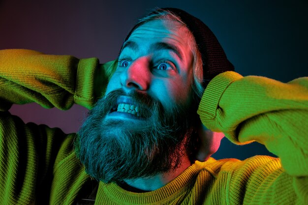 Exremely shocked, astonished. Caucasian man's portrait on gradient studio background in neon light. Beautiful male model with hipster style. Concept of human emotions, facial expression, sales, ad.