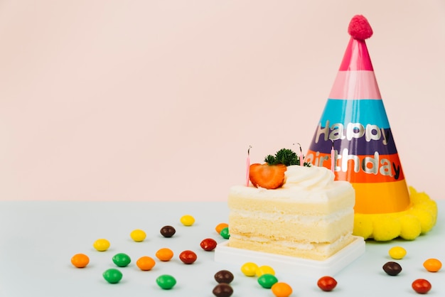 Extinguished candle on cake slice with candies and paper hat