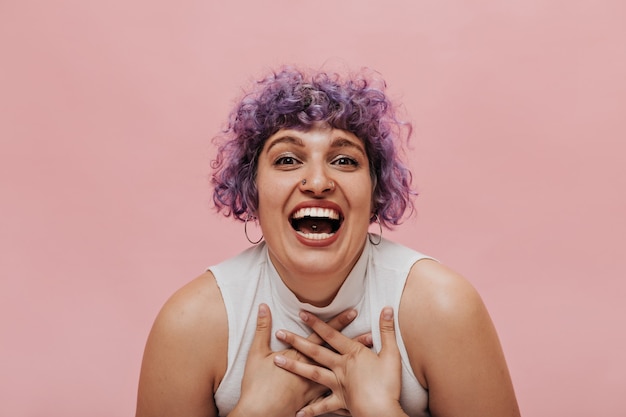 Free photo extraordinary woman with unusual purple hairstyle with piercings and earrings sincerely laughs on pink.