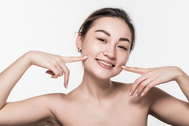 Extreme close up portrait of cute young asian woman pointing at wrinkles below cheek. Girl with charming smile and healthy white teeth isolated on white wall.