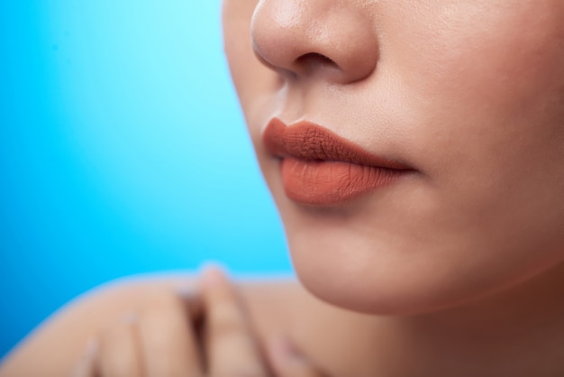 Extreme closeup of female mouth with lipstick, nose, and fingers touching bare shoulder, on blue