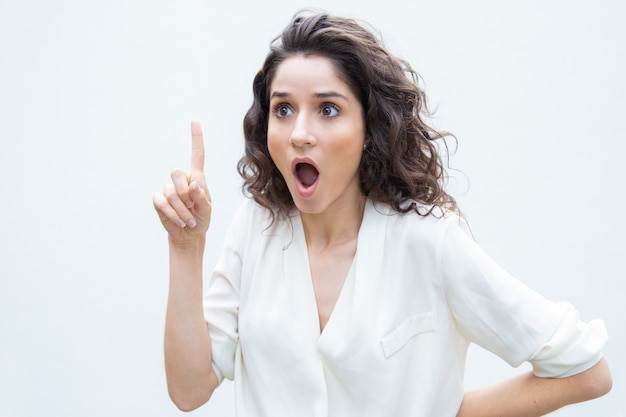 Free photo extremely amazed woman gasping, pointing finger up