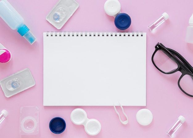 Eye care accessories on pink background with notebook mock-up