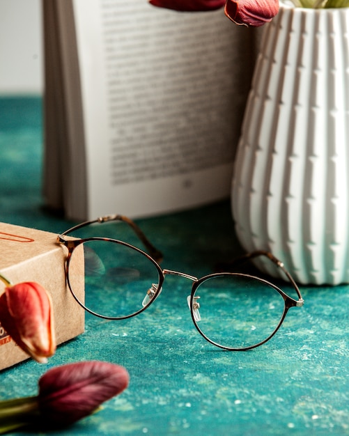 Foto gratuita occhiali libro vaso e tulipani sul tavolo