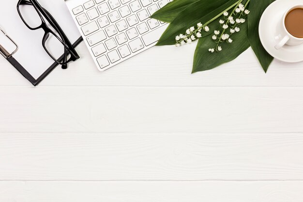 Free Photo eyeglasses,clipboard,keyboard,flower and leaves with coffee cup on office desk