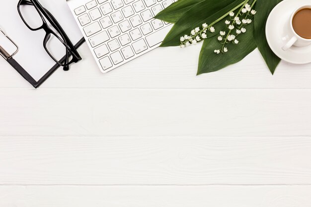 Eyeglasses,clipboard,keyboard,flower and leaves with coffee cup on office desk