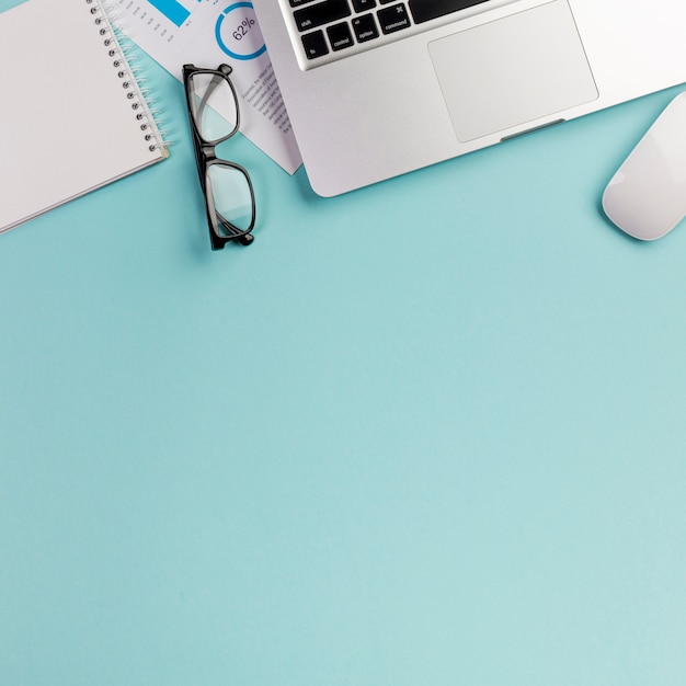 Eyeglasses,laptop,mouse and spiral notepad on office desk