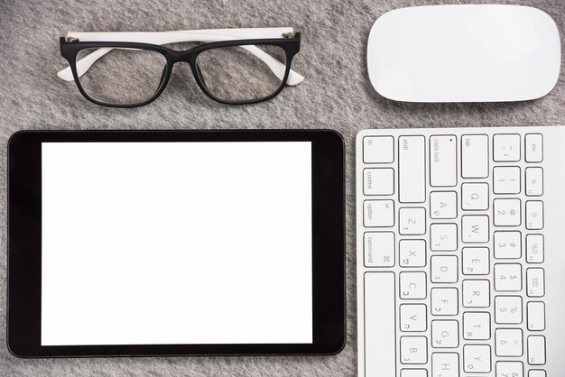 Eyeglasses; mouse; keyboard and digital tablet with blank white screen display on gray table top