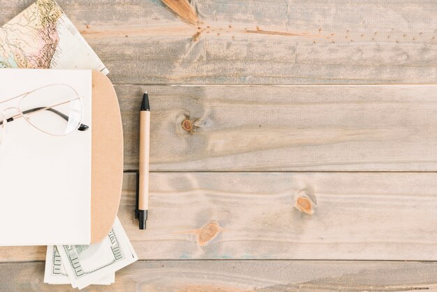 Eyeglasses; notepad; currency; map and pen on wooden plank background