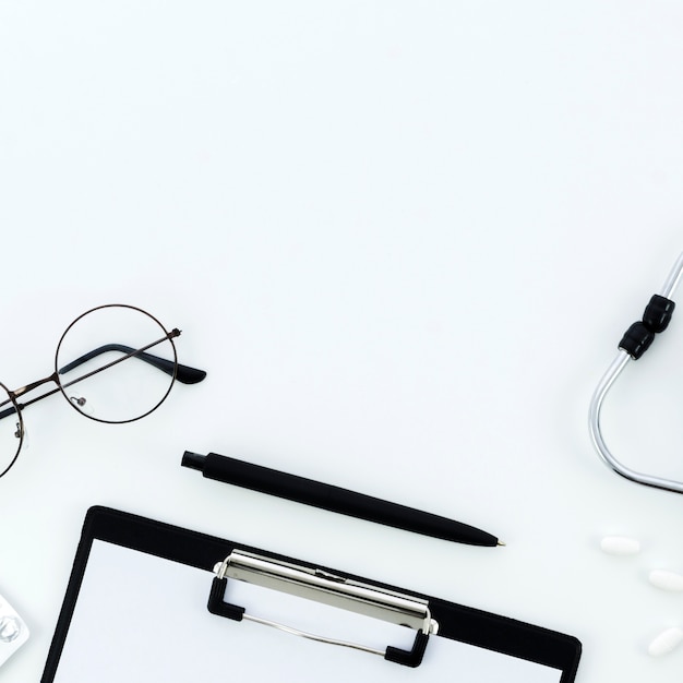 Очки; ручка; буфер обмена; таблетки и стетоскоп на белом фоне