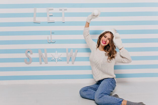 Eyes of cute girl glow with happiness in anticipation of fun game of snowballs. Model photo in jeans on striped wall