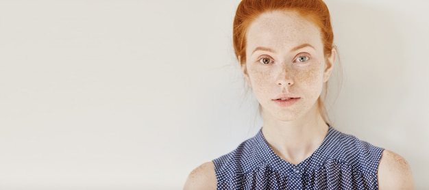 Free photo eyes of different colors: blue and brown. tender freckled young caucasian female with heterochromia iridum wearing sleeveless shirt with spots having rest indoors, looking with faint smile