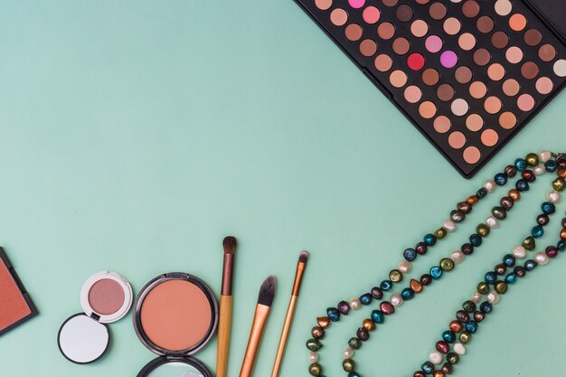 Free photo eyeshadow palette; beads necklace; blusher with makeup brushes on pastel backdrop