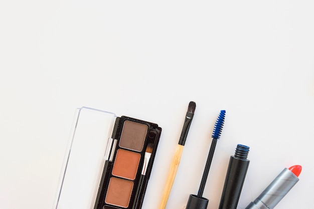 Eyeshadow palette; brush; red lipstick and mascara on white backdrop