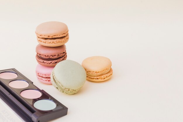Eyeshadow palette and stack of macaroons over beige background
