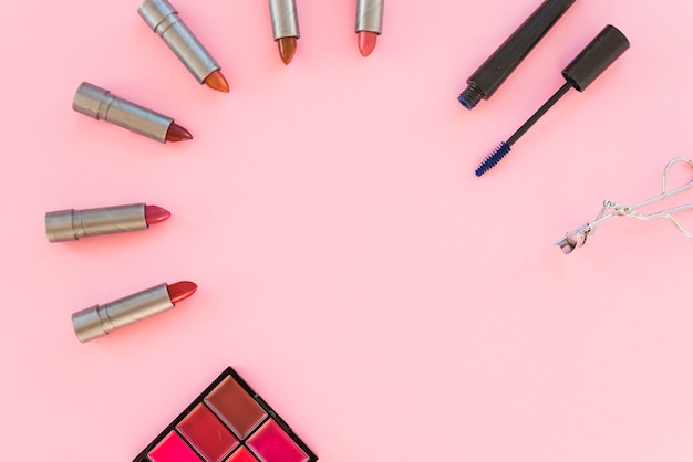 Eyeshadow palette; variety of lipstick shades; mascara; arranged over pink background