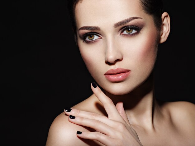 Face of a beautiful girl with fashion makeup and black nails posing at studio over dark background